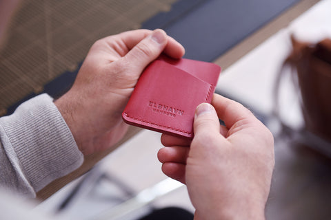 Nahaufnahme von Händen mit Fokus auf dem roten Leder Kartenetui "Pocket Folio", die ihr elegantes Design und ihre Handwerkskunst in einer minimalistischen Umgebung zur Schau stellt.