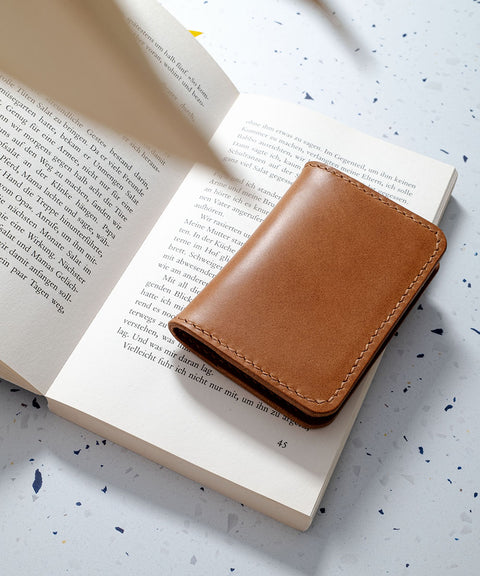 Kompaktes Kartenetui "Folio" in Cognacfarbe liegend auf einem geöffneten Buch, stilvoll und minimalistisch.