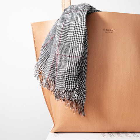 Leder Shopper-Tasche "Vacchetta Tote" von ELBHAVN mit einem stilvollen karierten Schal darüber, der minimalistische Eleganz ausstrahlt.
